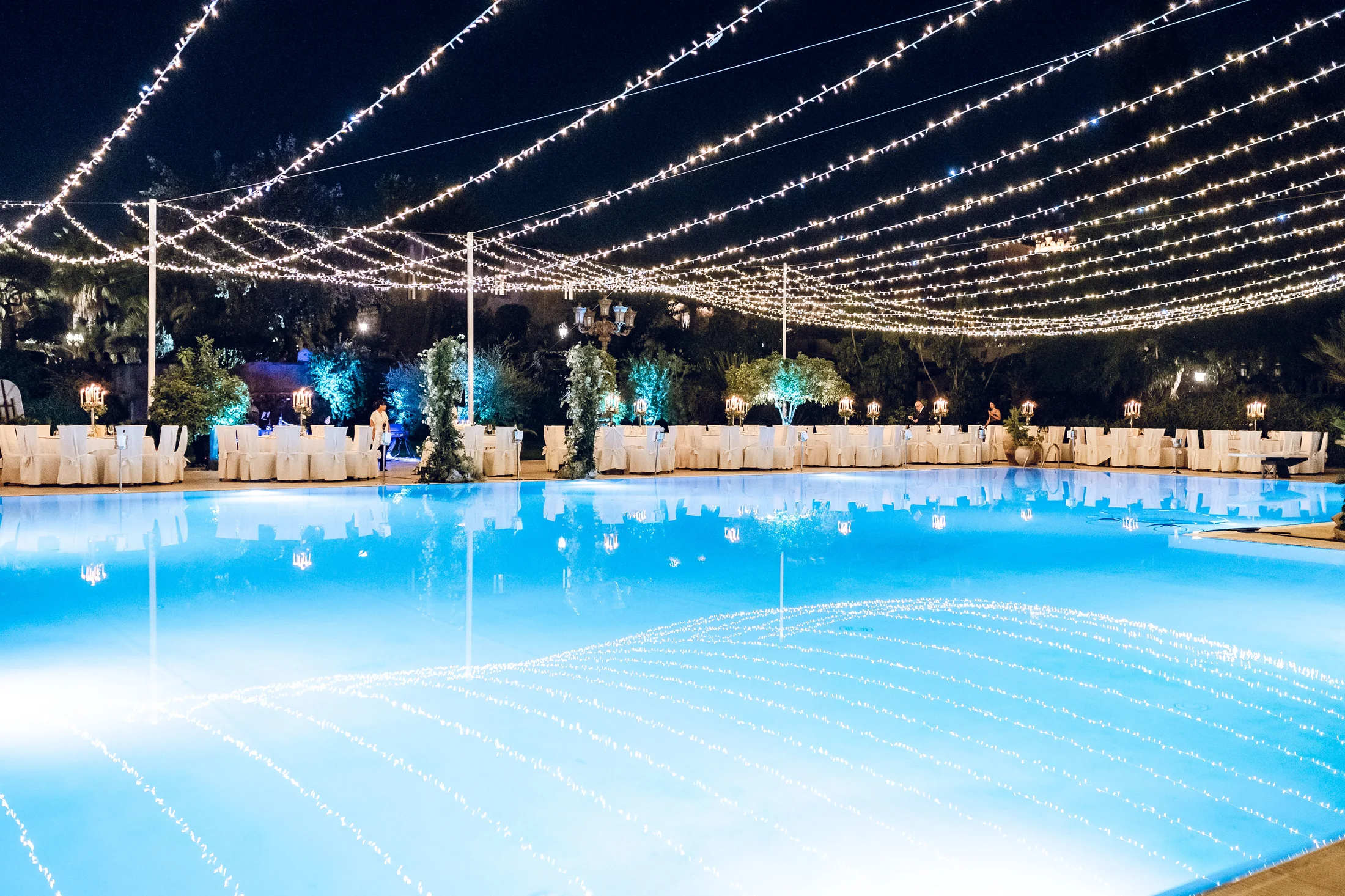 Evening reception beside a pool beneath string lights
