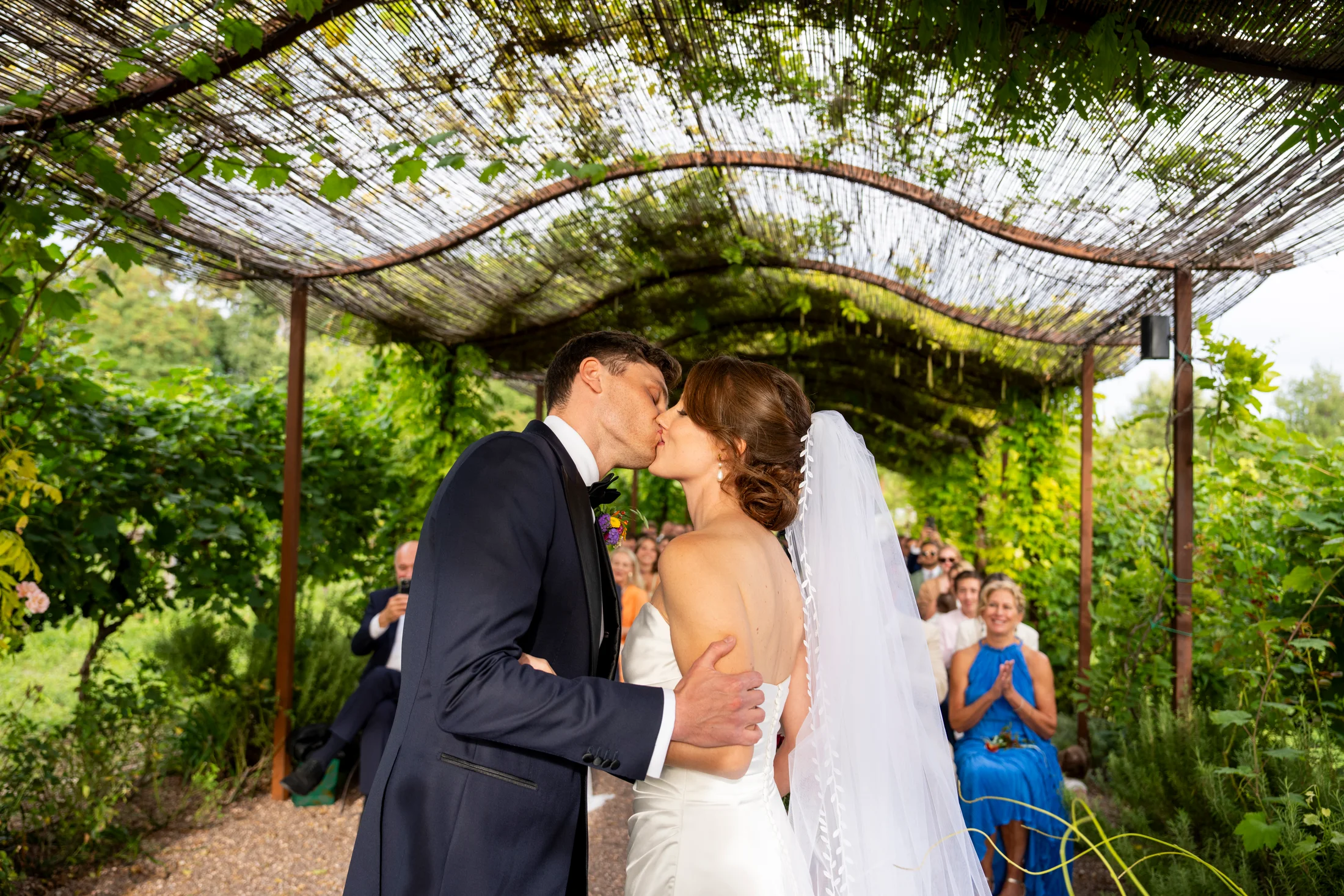 Bride and groom kissing beneath a leafy pergola