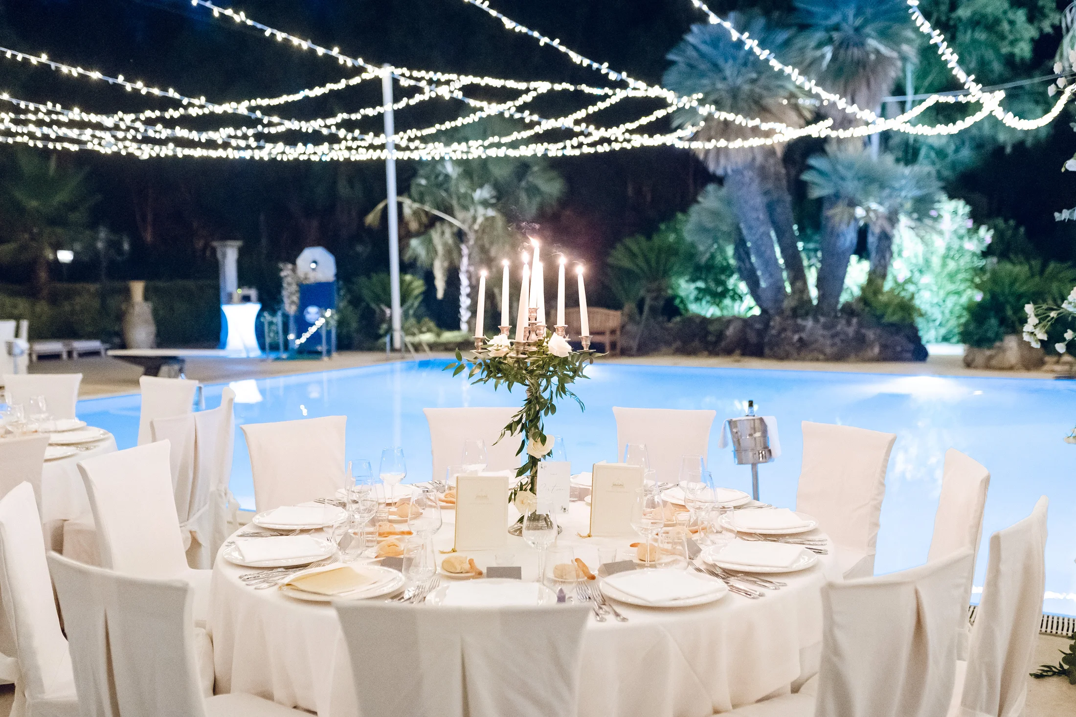 Reception tables beside a pool under string lights