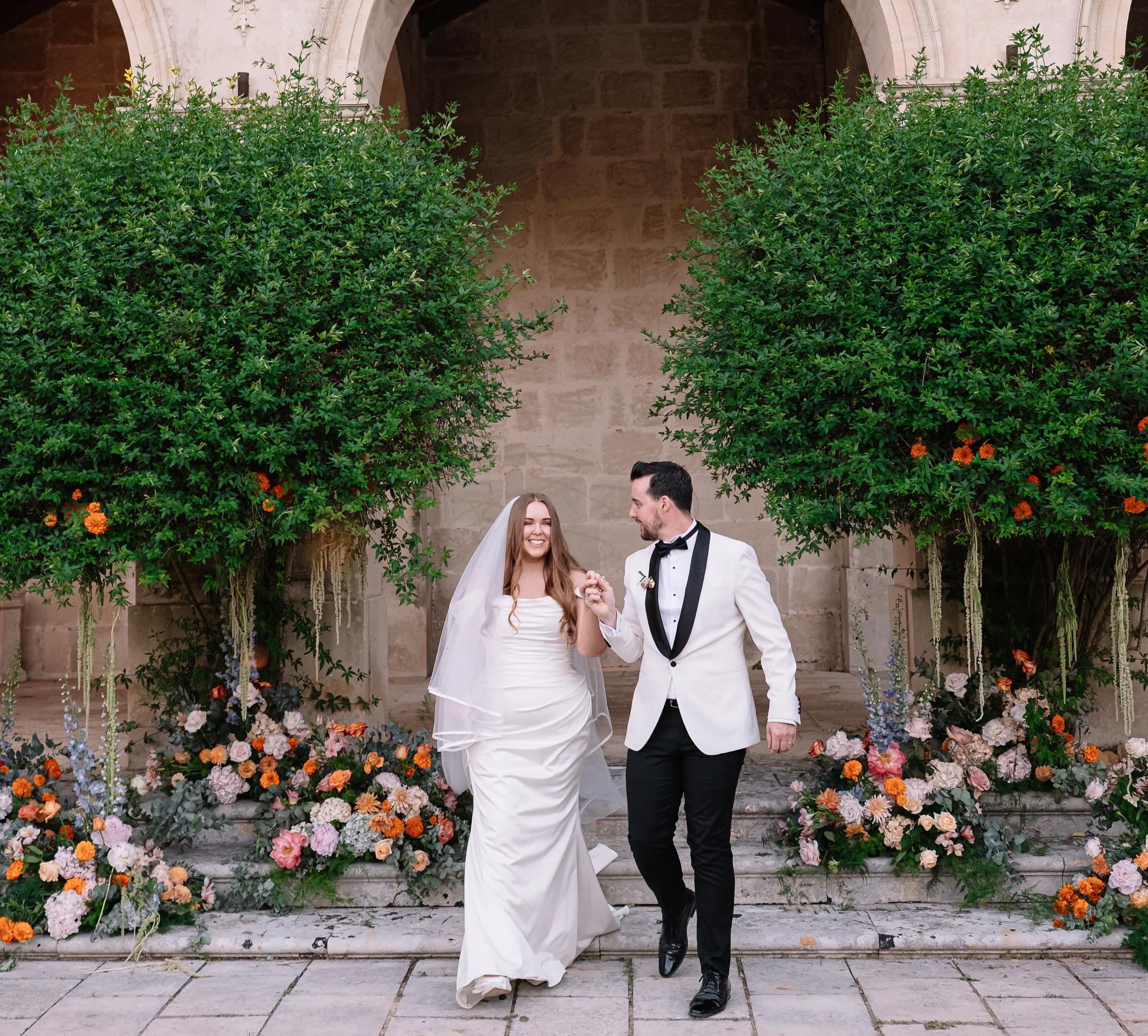 Bride and groom crossing a flower-filled courtyard