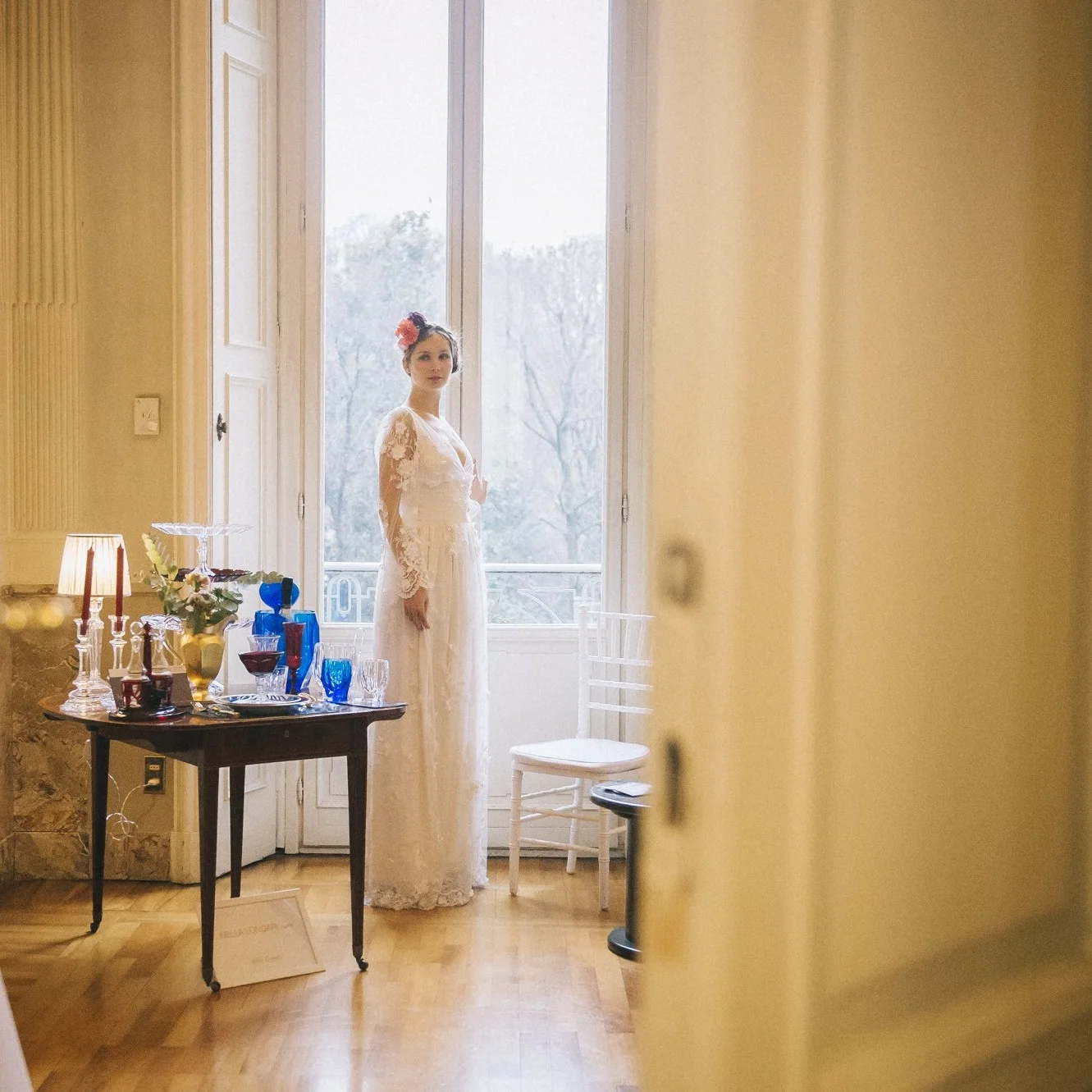 Bride standing in a sunlit room beside an open window